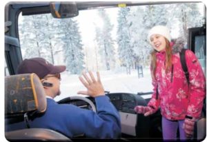 Talvinen kuva, jossa oppilas astuu koulubussiin ja bussikuski tervehtii oppilasta kättä heiluttaen.