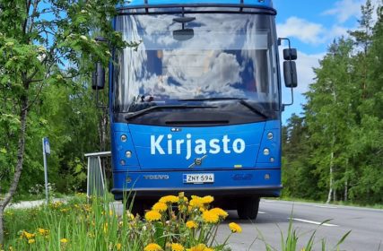 Kirjastoauton edessä rivissä keltaisia voikukkia.