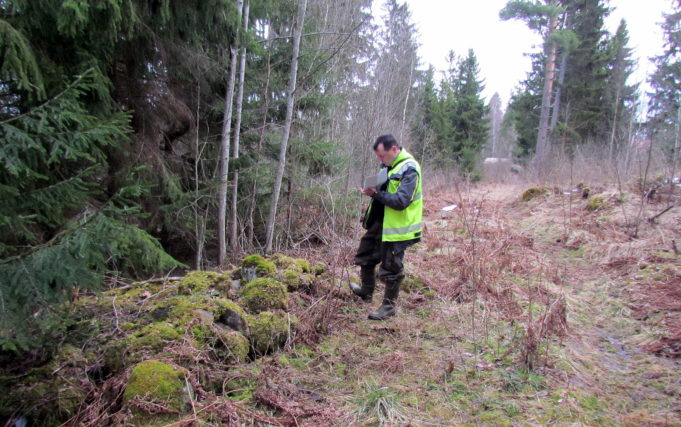 Huomioliiviin pukeutunut mieshenkilö seisoo metsäaukealla ja tekee muistiinpanoja.