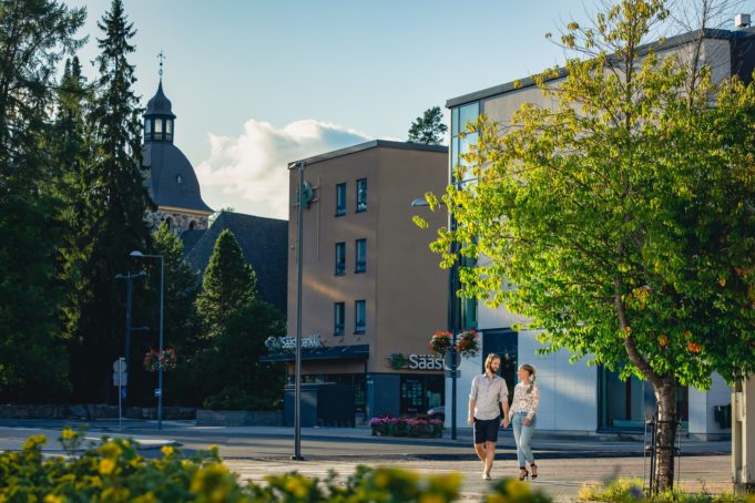 Mies ja nainen kävelevät käsi kädessä Kangasalan kesäisessä keskustassa, taustalla näkyy kirkko.