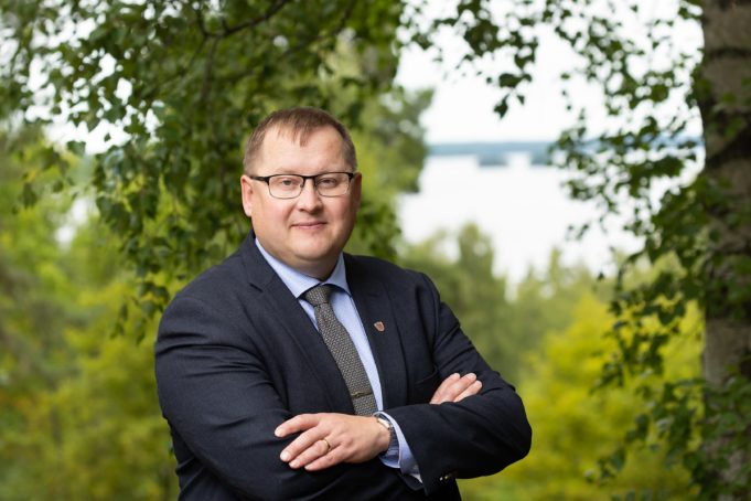 Kaupunginjohtaja Oskari Auvinen seisoo harjunlaella, taustalla näkyy kesäisiä lehtipuita ja järvimaisema.
