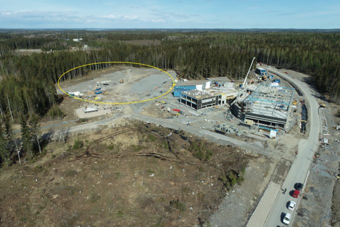 Ilmakuva, jossa näkyy metsää ja rakennustyömaata. Metsän reunassa on aukea alue, johon tuleva liikunapuisto on merkitty keltaisella ympyrällä.