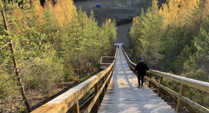 Tummiin ulkoiluvaatteisiin pukeutunut henkilö kävelee portaita alas kohti Sorolan monttua. Portaiden molemmilla puolilla näkyy metsää.