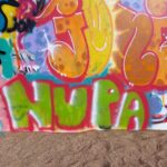 Hiekalla pystyssä oleva taulu, jossa graffitimaalaus, jossa lukee NUPA