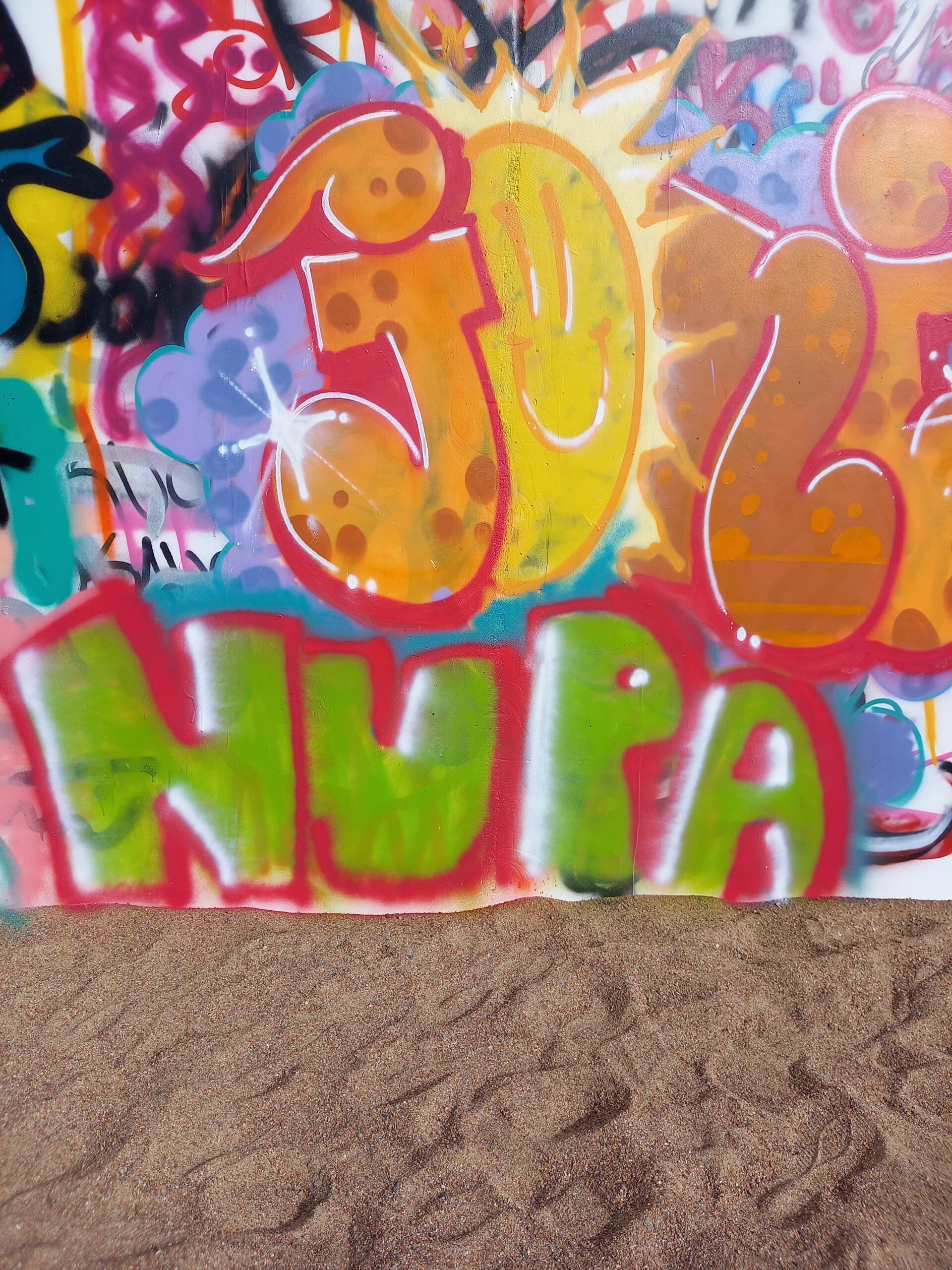 Hiekalla pystyssä oleva taulu, jossa graffitimaalaus, jossa lukee NUPA