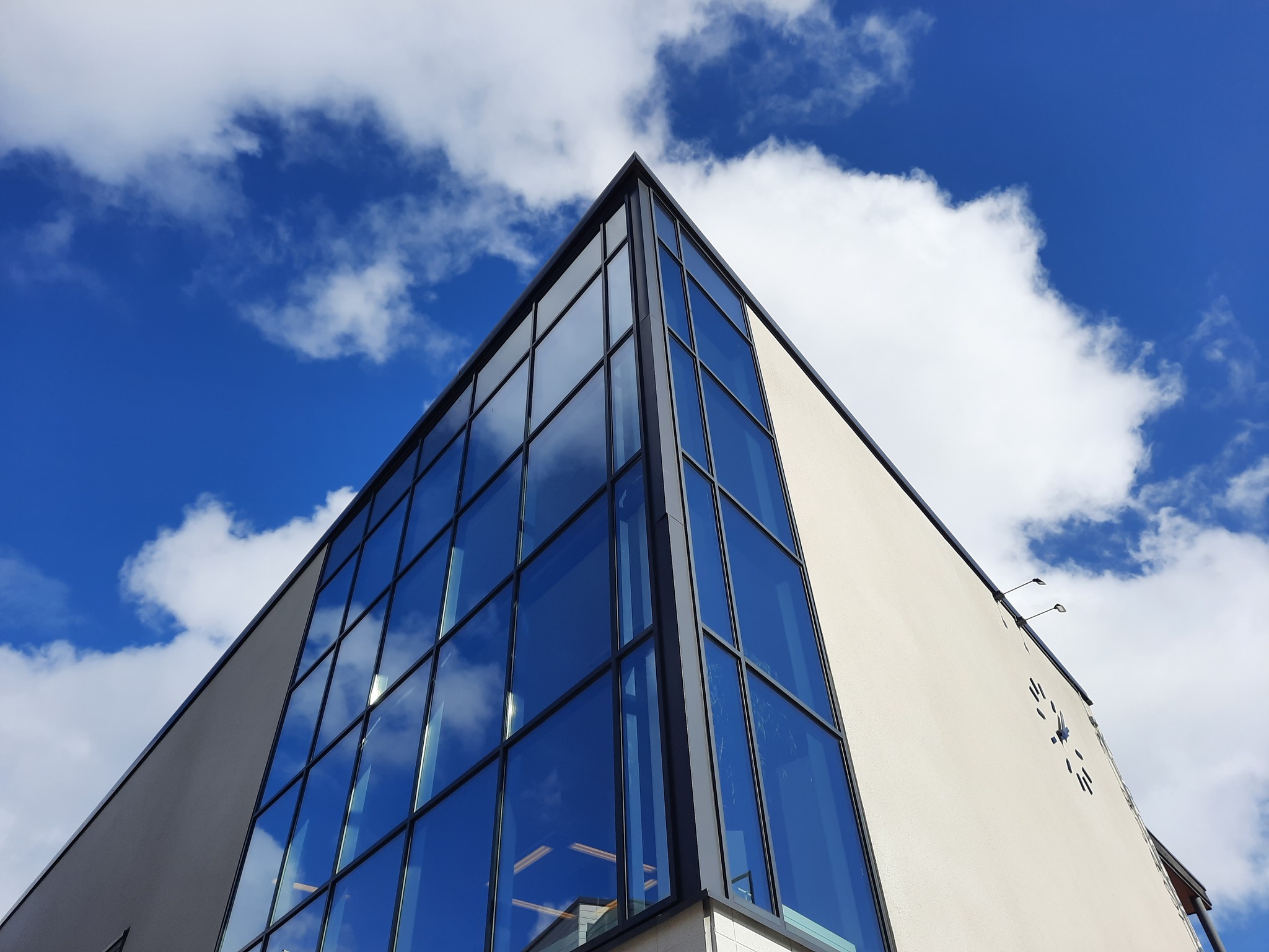 Alhaalta päin kuvattuna pääkirjaston lasiseinäinen kulma. Taustalla sininen taivas ja poutapilviä.