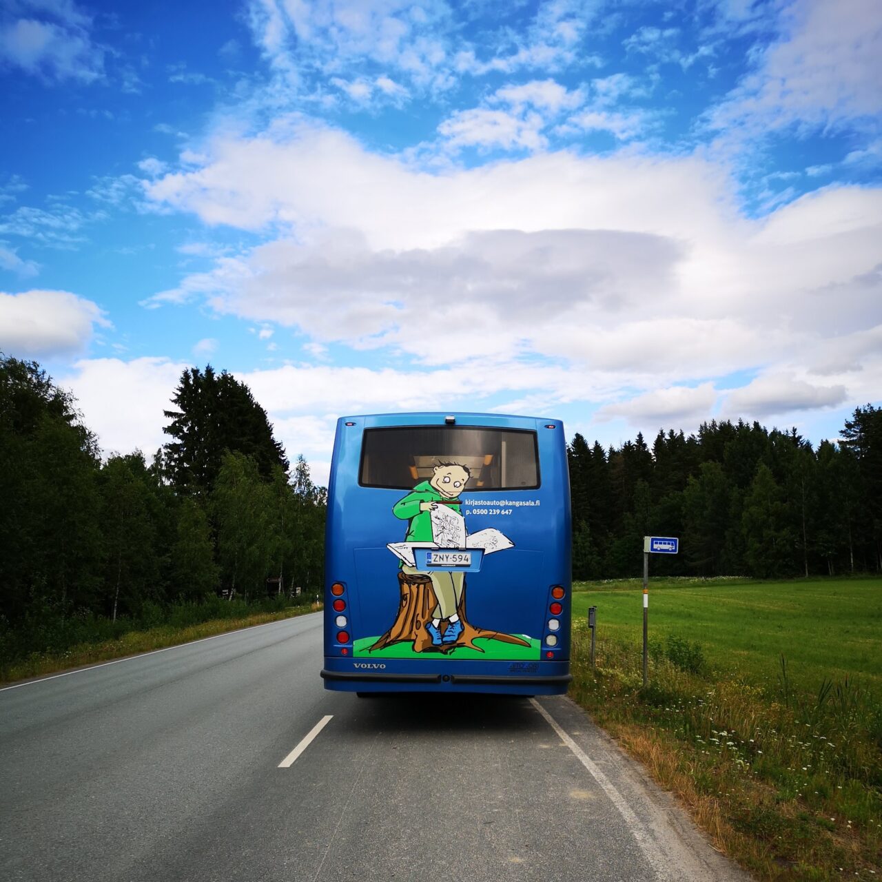 Kangasalan kirjastoauto Kotikujan Konsta takaapäin kesäisessä maalaismaisemassa.