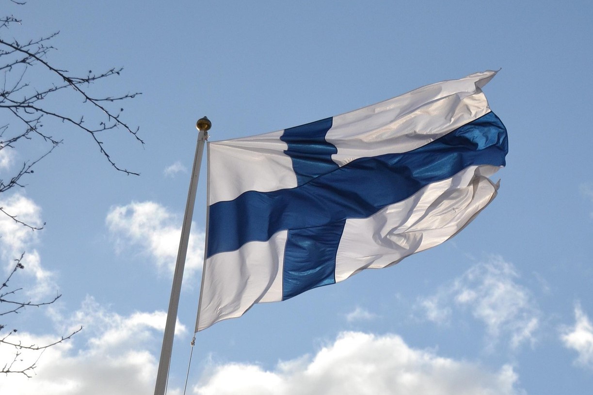 Suomen lippu liehuu tuulessa sinistä taivasta vasten.