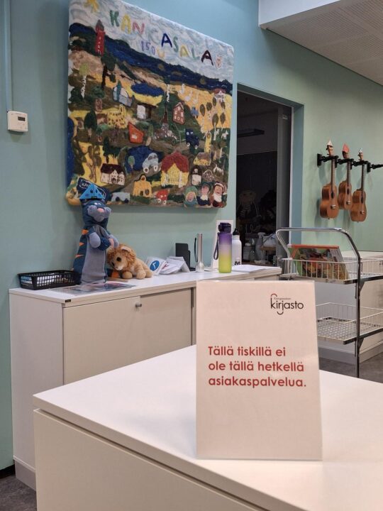 Kirjaston lastenosaston asiakaspalvelutiski, jolla on lappu: Tällä tiskillä ei tällä hetkellä ole asiakaspalvelua.
