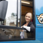 Kirjastoauton kuljettaja kurkkaa hymyillen avoimena olevasta kirjastoauto Kotikuja Konstan etuikkunasta.