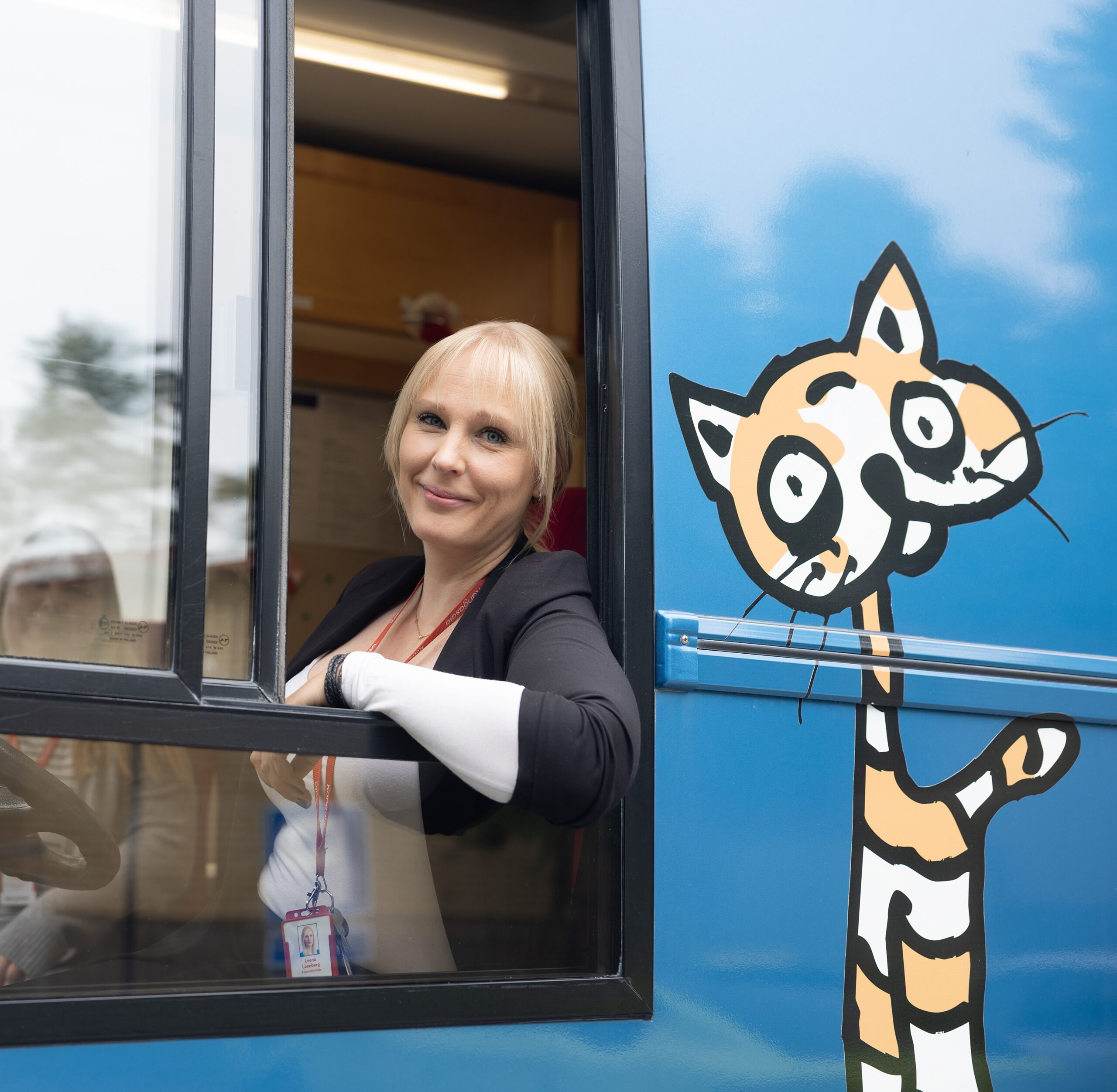 Kirjastoauton kuljettaja kurkkaa hymyillen avoimena olevasta kirjastoauto Kotikuja Konstan etuikkunasta.