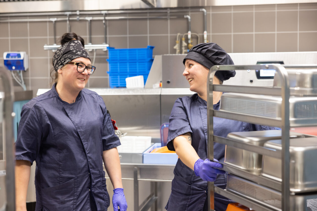 Kuvassa kaksi palvelutyöntekijää hymyilee