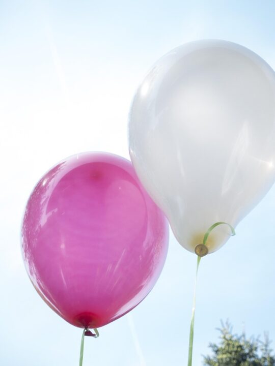 Vaaleaa taivasta vasten pinkki ja valkoinen ilmapallo.