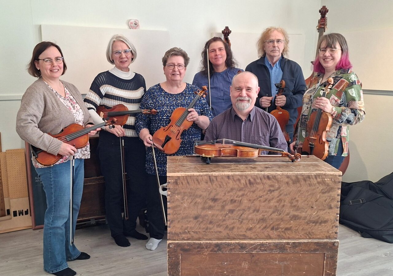 Hymyileviä aikuisia ihmisiä viulut käsissään. 