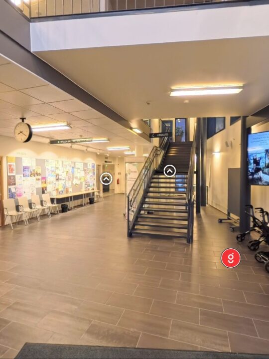 Kirjaston ala-aulaa virtuaalikierrokselta. Tilassa näkyy valkoisia ja punaisia painikkeita tilassa liikkumista ja lisätietojen hankkimista varten.